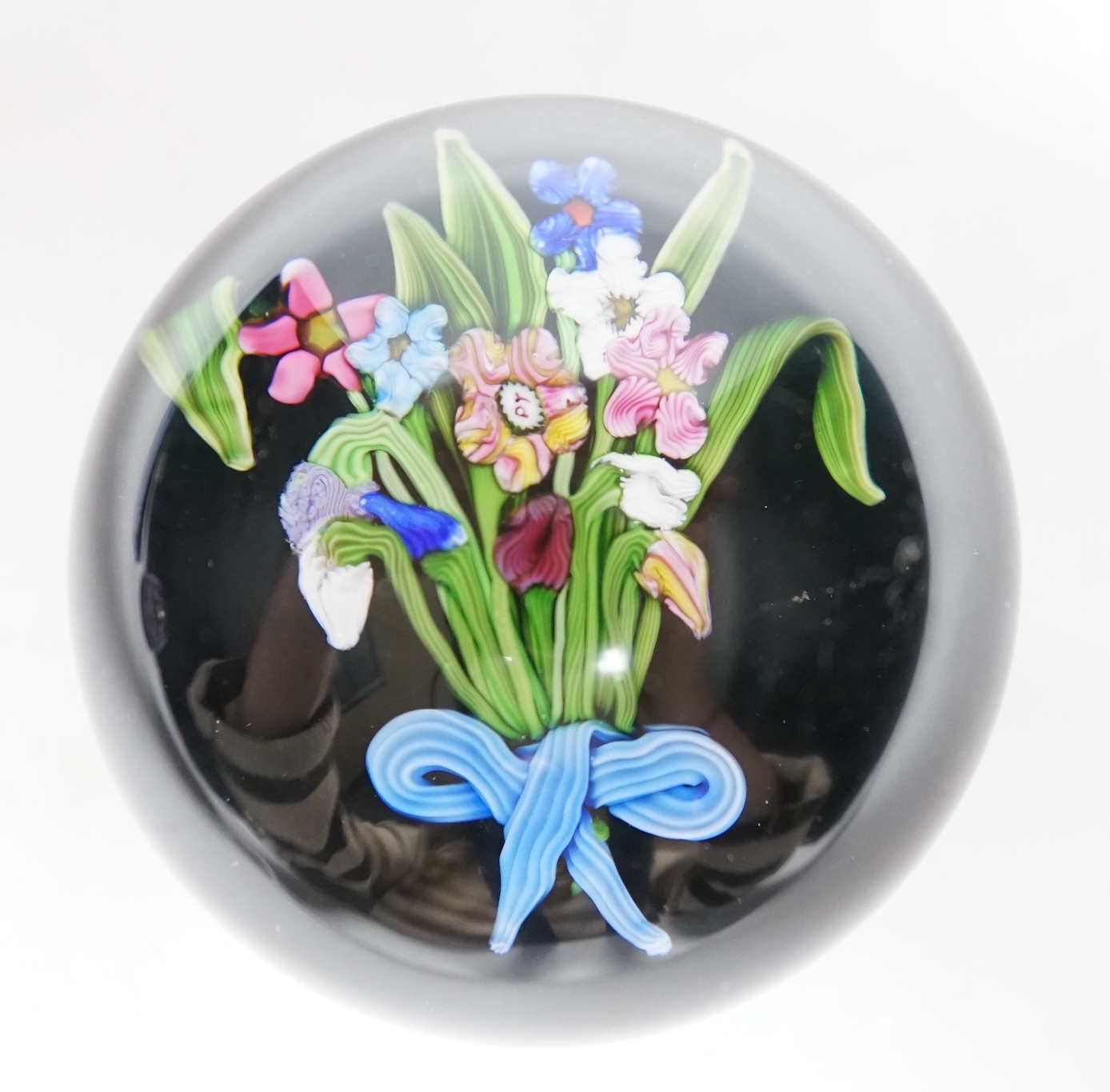 A Paul Ysart ‘small flower bouquet’ glass paperweight, pre-war Moncrieff period, ‘PY’ cane, the bouquet with a blue and white tied ribbon, black opaque ground, rough pontil, 6.5cm